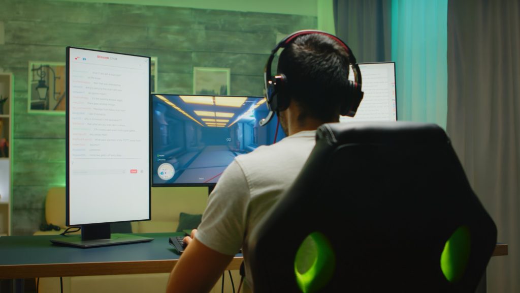 back view professional gamer streaming his competition triple monitor setup with two streaming chats open (1)