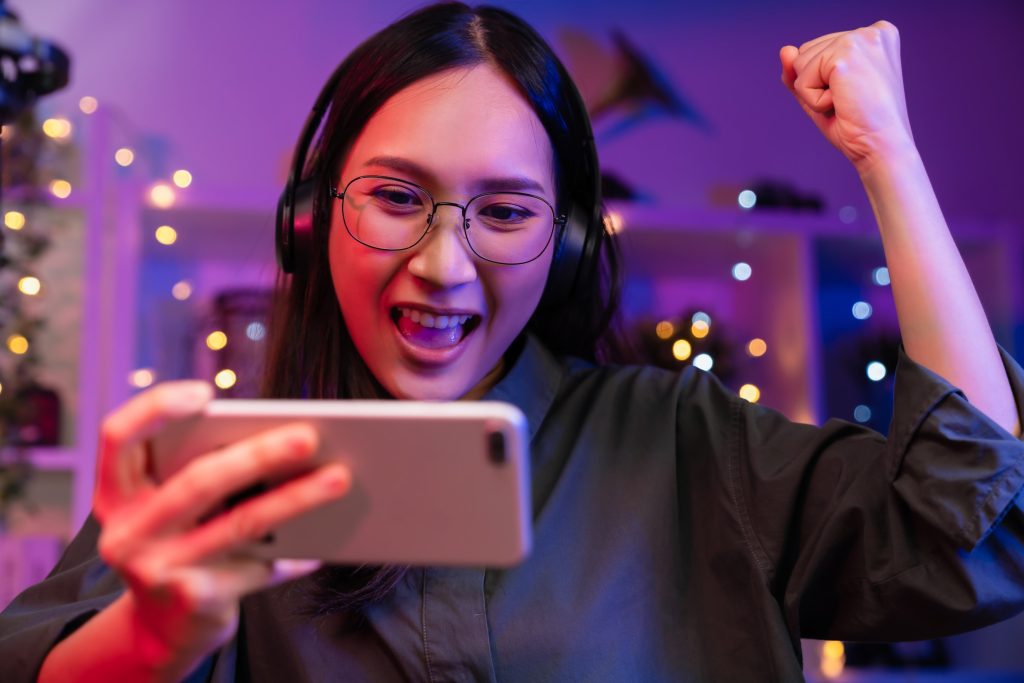 excited young asian woman wearing headset playing online game smartphone with live broadcasting internet (1)